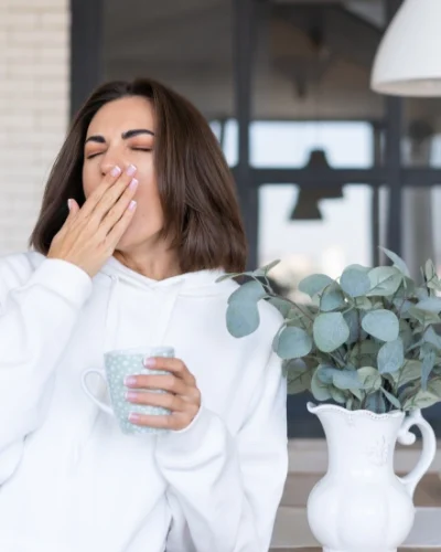yawning while holding a cup of coffee in morning