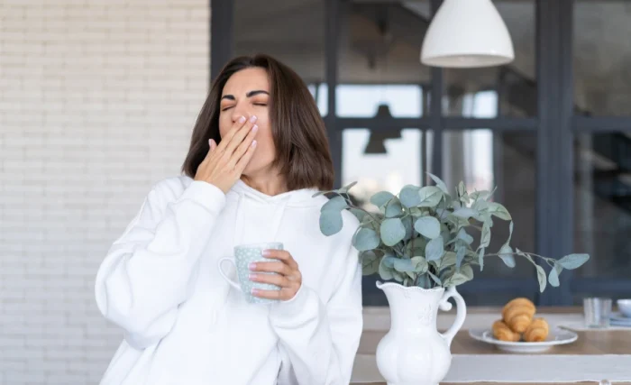 yawning while holding a cup of coffee in morning